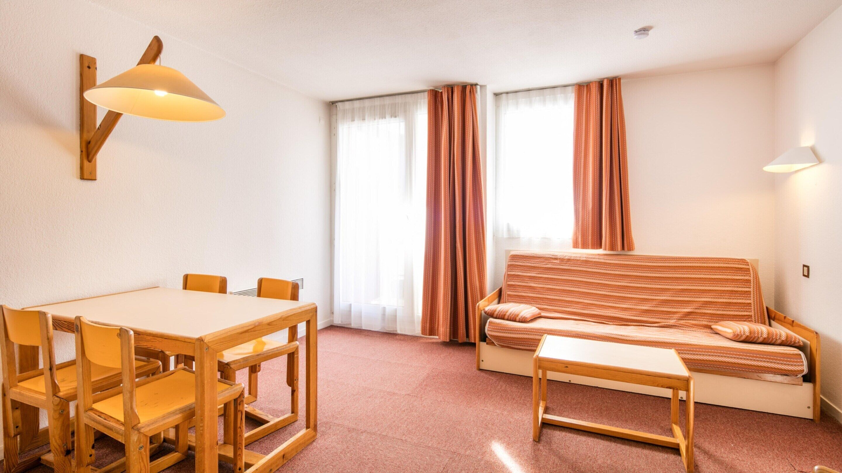 A room with a wooden table, chairs, a sofa, and a bed.