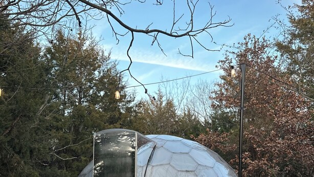 A geodesic dome structure with a transparent entrance, two wooden chairs, and a wooden deck.