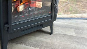 A portable stove with a glass window, placed on a wooden floor.