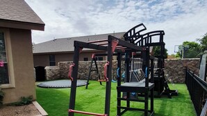 Une aire de jeux avec une structure d’escalade, des balançoires et un trampoline.