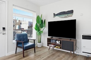 Ein Wohnzimmer mit Fernseher, Blumentopf, blauem Sessel und Wandverziierung mit Fischmotiv.