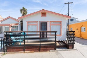 A small, single-story building with a red roof and white walls, featuring a front porch with a wooden bench and a small set of stairs leading up to the entrance. - Beach & Bay Escape | Prime Mission Spot (San Diego)