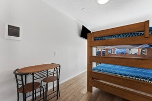 A bunk bed with a blue patterned mattress, a wooden bench with two seats, and a wall-mounted air vent. - Beach & Bay Escape | Prime Mission Spot (San Diego)