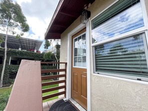 Ein Hauseingang mit einer Holztür, einem Fenster mit Rollläden und einer Veranda mit einer Bank.