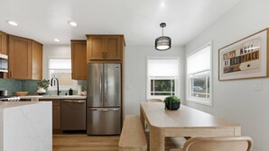 Une cuisine moderne avec des meubles en bois, un réfrigérateur en acier inoxydable, un îlot en marbre et un coin repas avec un banc.