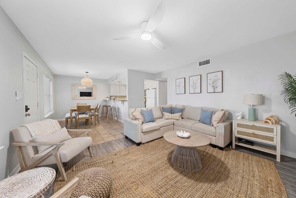 A modern living room with a sofa, coffee table, and a dining area with chairs. - Ocean Echo 103 (Gulf Shores)