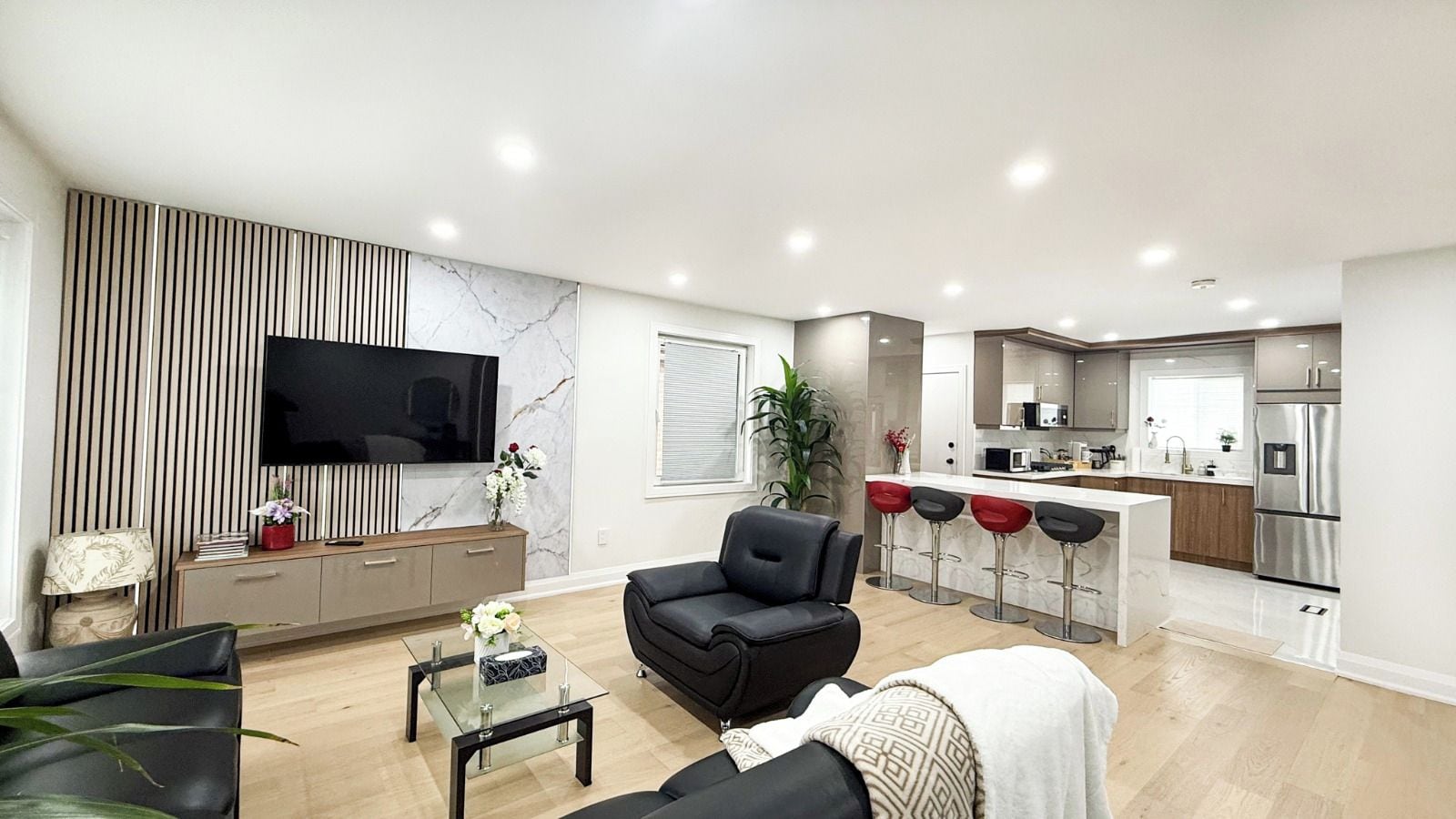 A modern living room with a flat-screen TV, a sofa, a coffee table, and a dining area with bar stools.