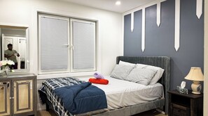 Une chambre à coucher avec un lit, une table de chevet, une lampe et une fenêtre avec des stores.