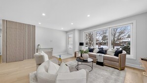 Ein modernes Wohnzimmer mit Sofa, Sesseln, einem Couchtisch und einem großen Fenster mit Blick auf eine verschneite Landschaft.