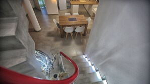 A staircase with a red handrail leading to a dining area with a wooden table and white chairs.