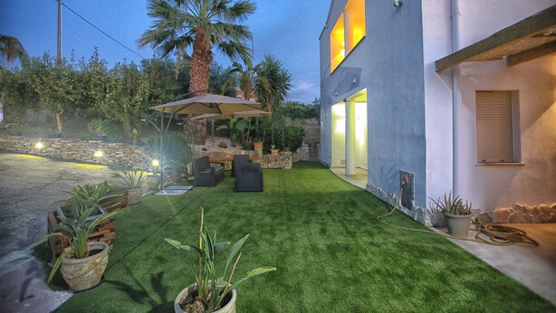 A modern outdoor patio with artificial grass, seating, and potted plants.