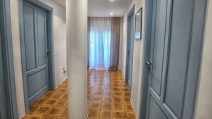 A corridor with blue doors, a tiled floor, and a view into a room with a curtain.