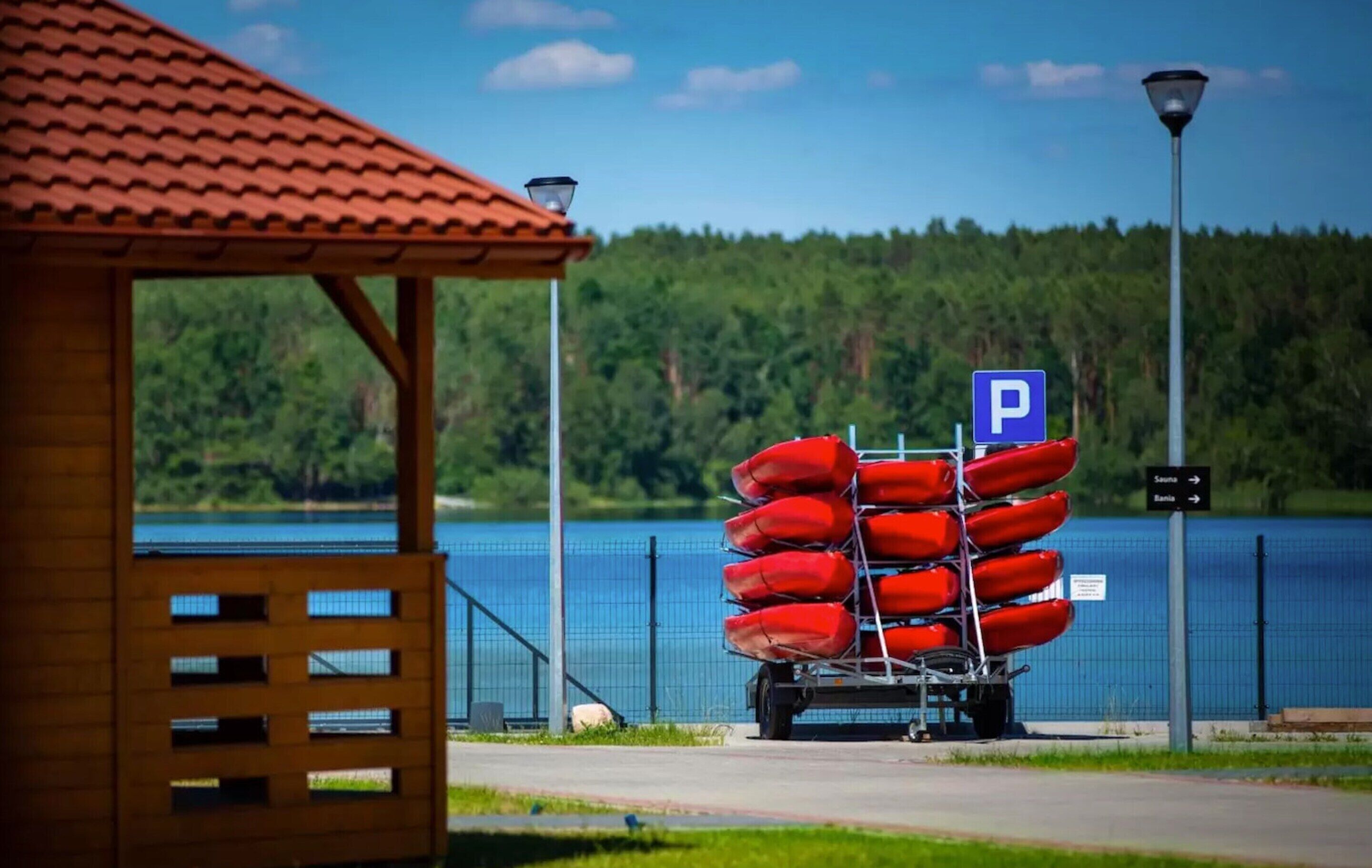 A wooden structure with a red roof, a blue parking sign, and a row of red life vests on a trailer by a lake.