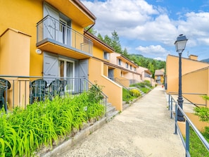 A row of yellow buildings with balconies, a gravel path, and green plants. - Spacious Alpine Triplex With Terrace (Guillaumes)
