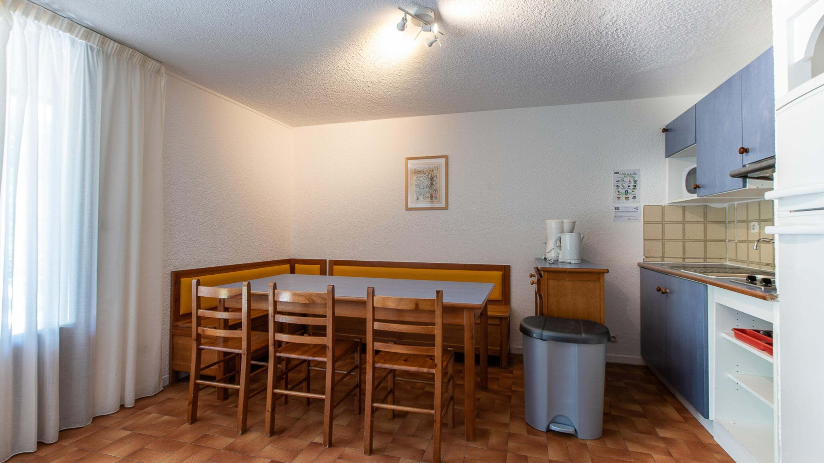 Une cuisine compacte comprenant une table à manger, des chaises, une poubelle et un coin cuisine.