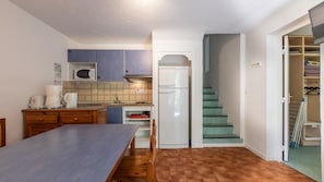 A compact kitchen with a microwave, coffee maker, and refrigerator, a wooden dining table, and a staircase leading to a closet. - Spacious Alpine Triplex With Terrace (Guillaumes)