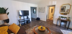 Ein Wohnzimmer mit Flachbildfernseher, Couchtisch und Sofa. Ein Flur führt in einen weiteren Raum.