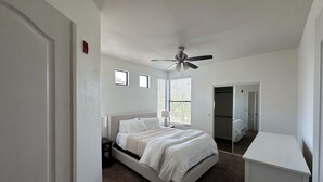 Ein Schlafzimmer mit einem Bett, einem Deckenventilator, einem Fenster mit Jalousien und einem Kleiderschrank.