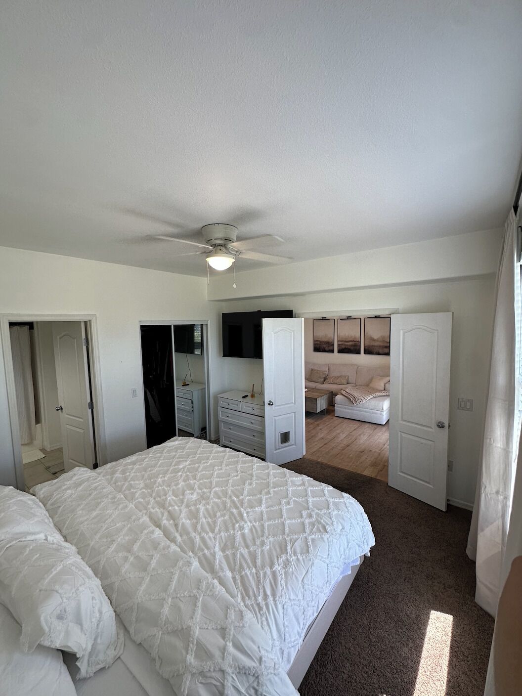 Une chambre dotée d’un grand lit, d’un ventilateur de plafond, d’un dressing et donnant sur un espace de vie avec un canapé.