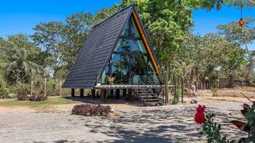 Una estructura de vidrio triangular moderna con una escalera de metal, rodeada por un paisaje natural.