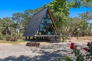 Una estructura de vidrio triangular moderna con una escalera de metal, rodeada por un paisaje natural.