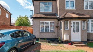 A two-story house with a car parked in the driveway, a satellite dish, and a small garden area. - Hounslow Hideaway Cottage (Hounslow)