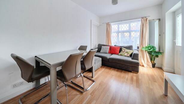 A modern living room with a dining table, chairs, a sofa, a potted plant, and a window with curtains. - Hounslow Hideaway Cottage (Hounslow)