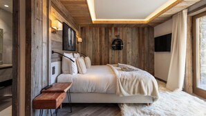 A bedroom with a wooden wall, a bed, a mounted TV, and a window with curtains. - Flocon - Ours Rouge: an exceptionally spacious apartment with a jacuzzi (Les Allues)