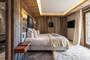 A bedroom with a wooden wall, a bed, a mounted TV, and a window with curtains. - Flocon - Ours Rouge: an exceptionally spacious apartment with a jacuzzi (Les Allues)