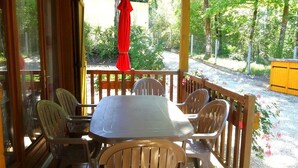 Een overdekt terras met een tafel en stoelen, omringd door een houten leuning en uitzicht op groen.