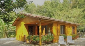 Une cabane en bois dotée d’une véranda, entourée de verdure.
