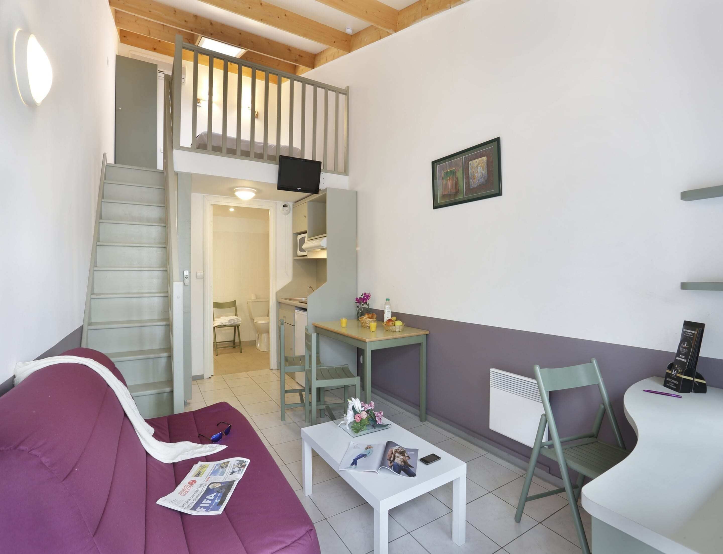 Un espace de vie compact comprenant un canapé, une petite table, une chaise, un escalier et un coin cuisine.