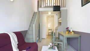 A compact living space with a sofa, a small table with a magazine and a phone, a staircase, and a television on the upper level. - Large Mezzanine Stay for 6 in Merville (Merville)