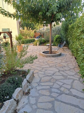A stone patio with a tree, a bench, and various plants. - New on Abritel: Newly built vacation home with a pool   (Vaison-la-Romaine)
