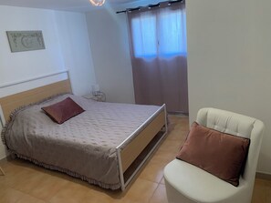 A bedroom with a bed, a chair, a nightstand, a wall-mounted lamp, and a window with curtains. - New on Abritel: A recently built vacation rental with a pool (Vaison-la-Romaine)