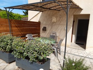 Eine Terrasse im Freien mit Tisch und Stühlen, umgeben von Pflanzkästen mit Grünpflanzen.