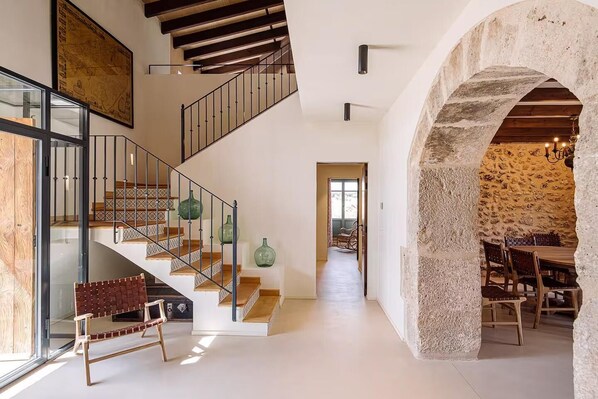 A spacious interior with a staircase, a dining area with rustic stone walls, and a view through an archway. - Son Seriol · Exclusive ECO Villa in Finca w/ views (Inca)