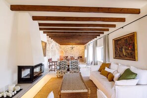A room with a white sofa, patterned armchairs, a woven bench, a stone wall, and a painting on the wall. - Son Seriol · Exclusive ECO Villa in Finca w/ views (Inca)