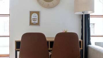 Una stanza con una scrivania in legno, due sedie marroni, una sveglia a muro, una lampada e un segnale WiFi incorniciato.