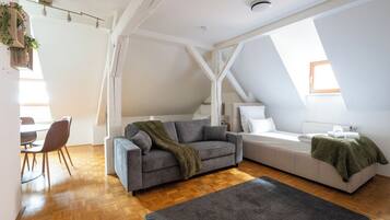 A loft-style room with a sofa, a bed, a dining area, and a staircase.