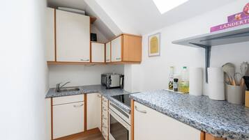 A compact kitchen with a microwave, toaster, and a small oven. There is a sink with a faucet, and a countertop with various kitchen items.