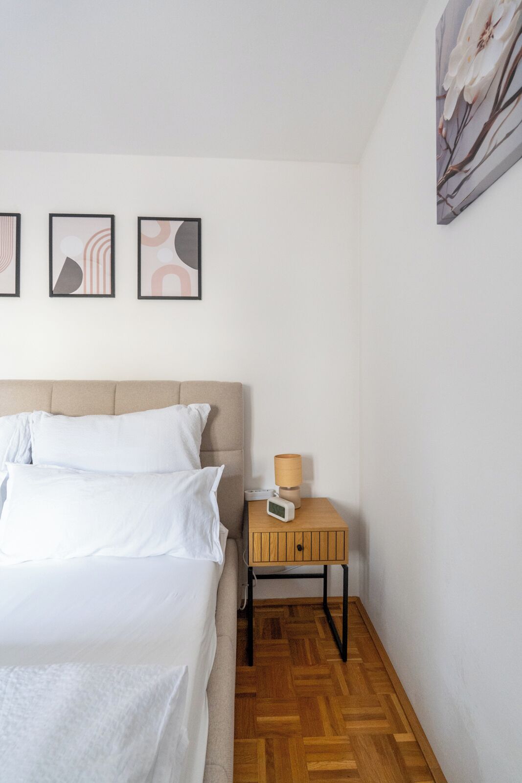 A bedroom with a bed, a nightstand with a lamp, and three abstract wall art pieces.