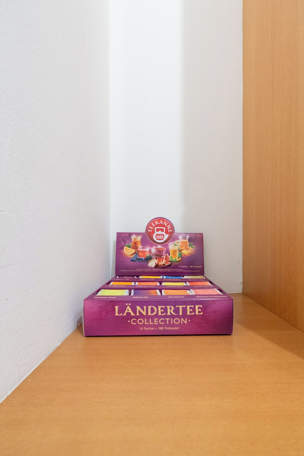 Una caja con varias cajas de té Ländertee Collection sobre una superficie de madera frente a una pared blanca.