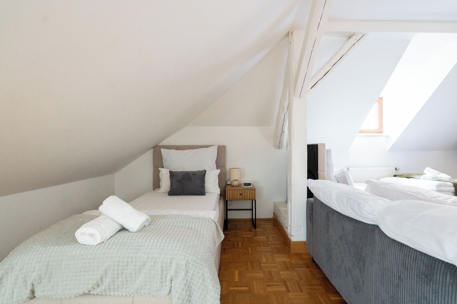 Een knus, goed verlichte zolderkamer met twee bedden, een nachtkastje en een houten vloer.