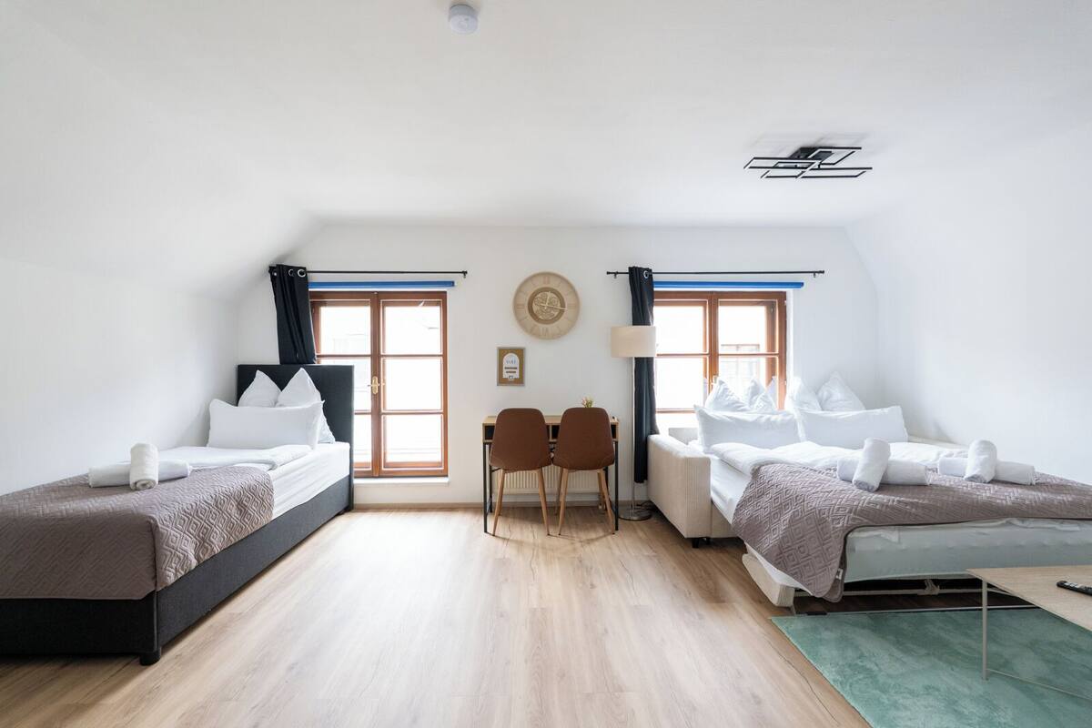 Una habitación con dos camas, un escritorio, dos sillas, un reloj y un ventilador de techo.