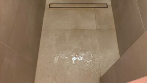 Ducha con cabezal de ducha de mano, panel de control empotrado en la pared y suelo de baldosas.