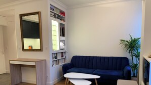 Una sala de estar con un sofá azul oscuro, una mesa de centro blanca, un escritorio pequeño y una estantería.