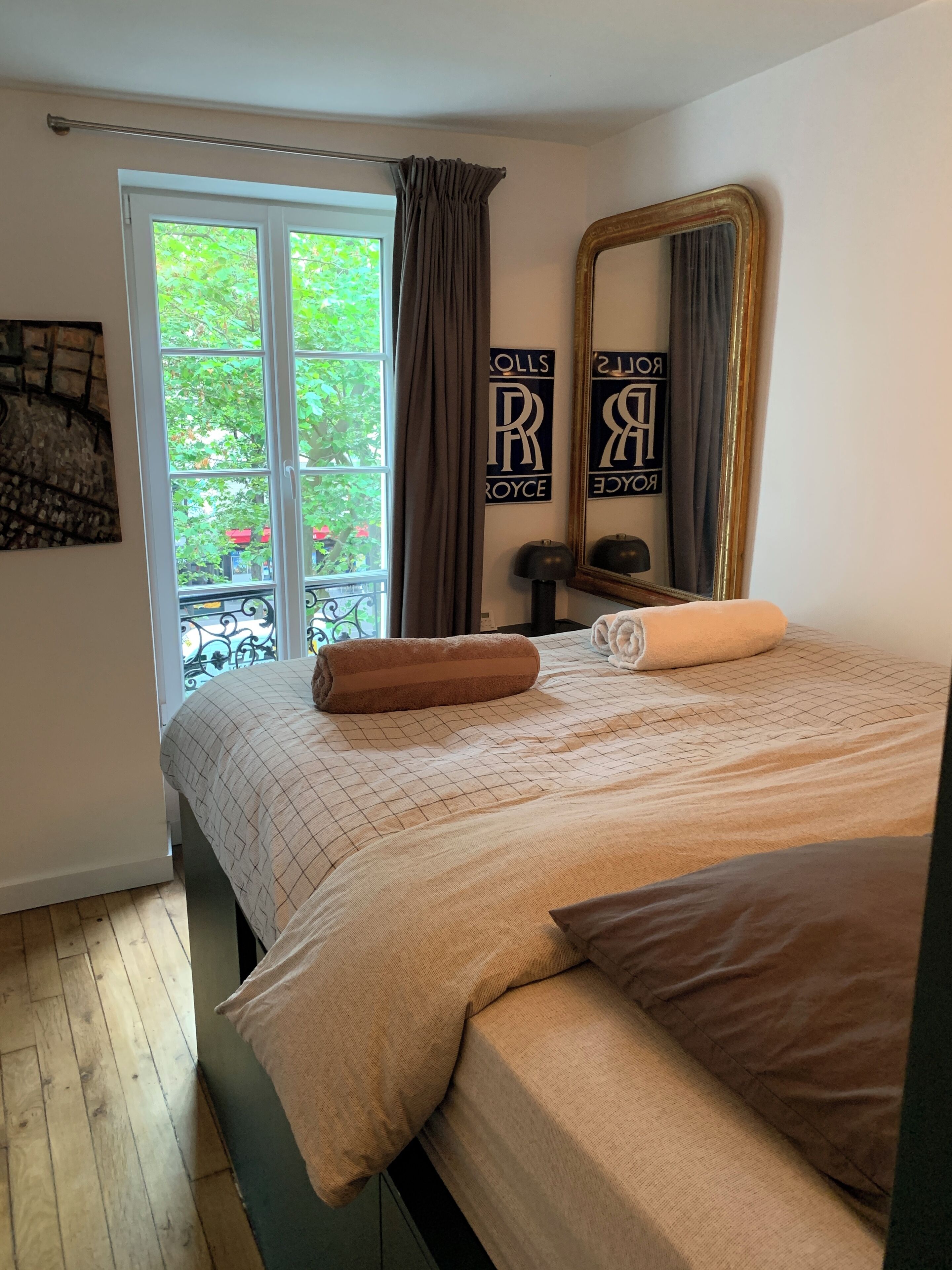 Een slaapkamer met een bed, een raam met gordijnen, een spiegel en een wand met een naambordje.
