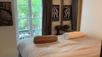 Een slaapkamer met een bed, een raam met gordijnen, een spiegel en een wand met een naambordje.