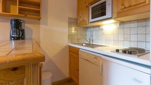 Kompakti keittiö, jossa on puukaapit, mikroaaltouuni, kahvinkeitin, pesuallas ja astianpesukone.